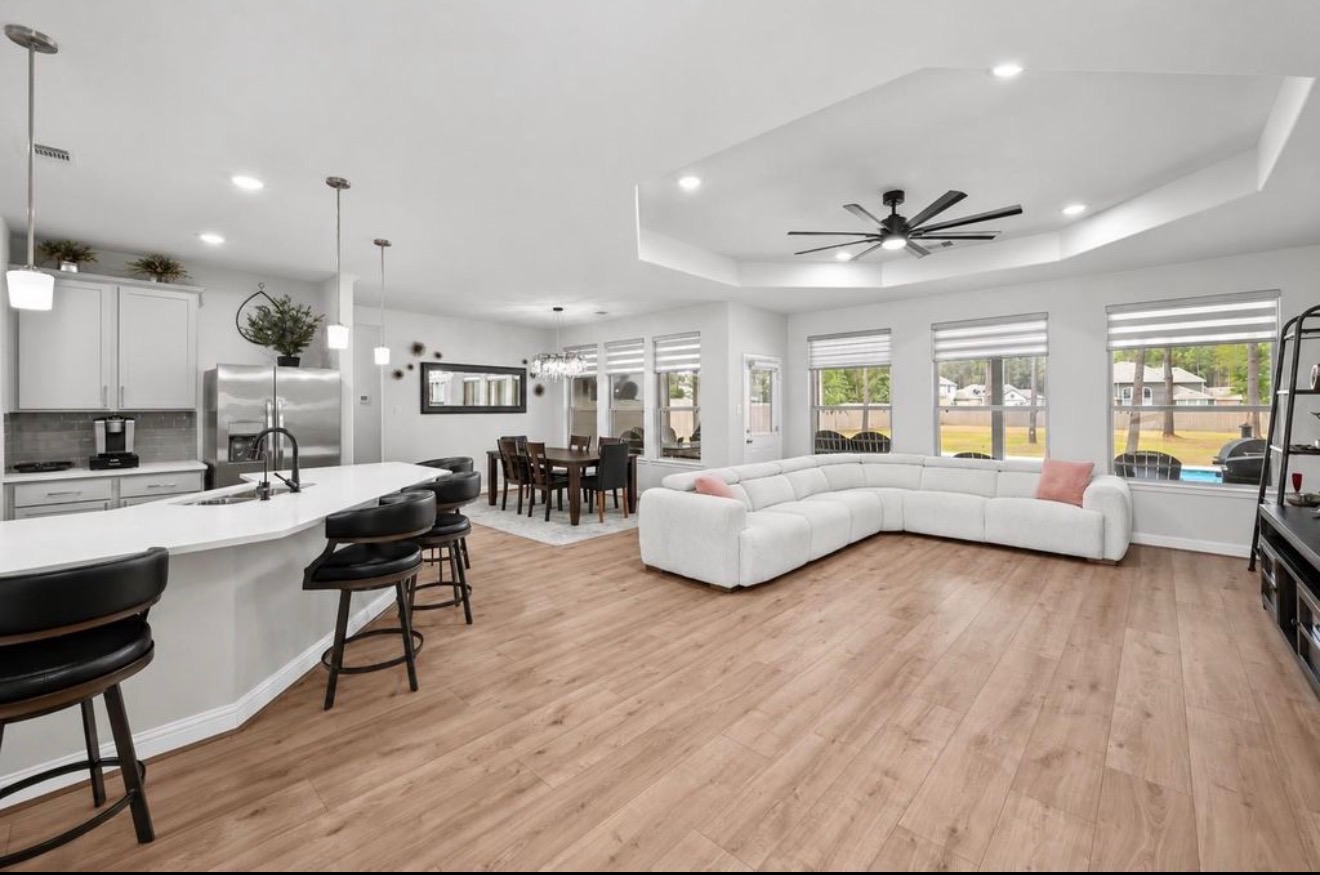 Bright open-plan living room with white sofas, wood floors, and a kitchen island